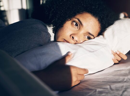 Eine Frau liegt wach im Bett und leidet unter Schlafproblemen, während sie auf einem Kissen ruht