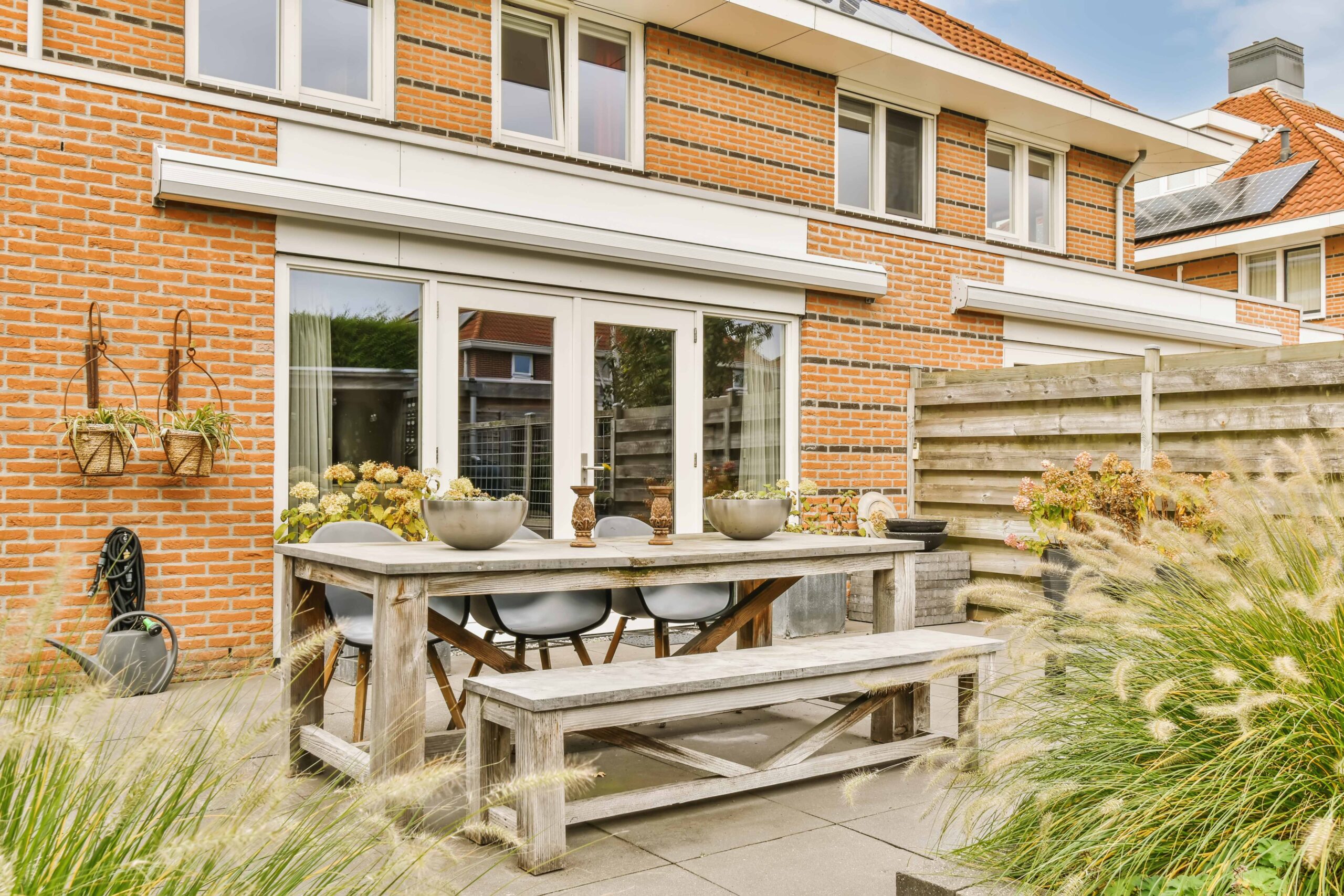 Outdoor-Sitzbank ohne Lehne an einem Esstisch auf einer Terrasse, umgeben von Pflanzen und Ziegelmauerwerk, ideal für gemütliche Mahlzeiten im Freien.