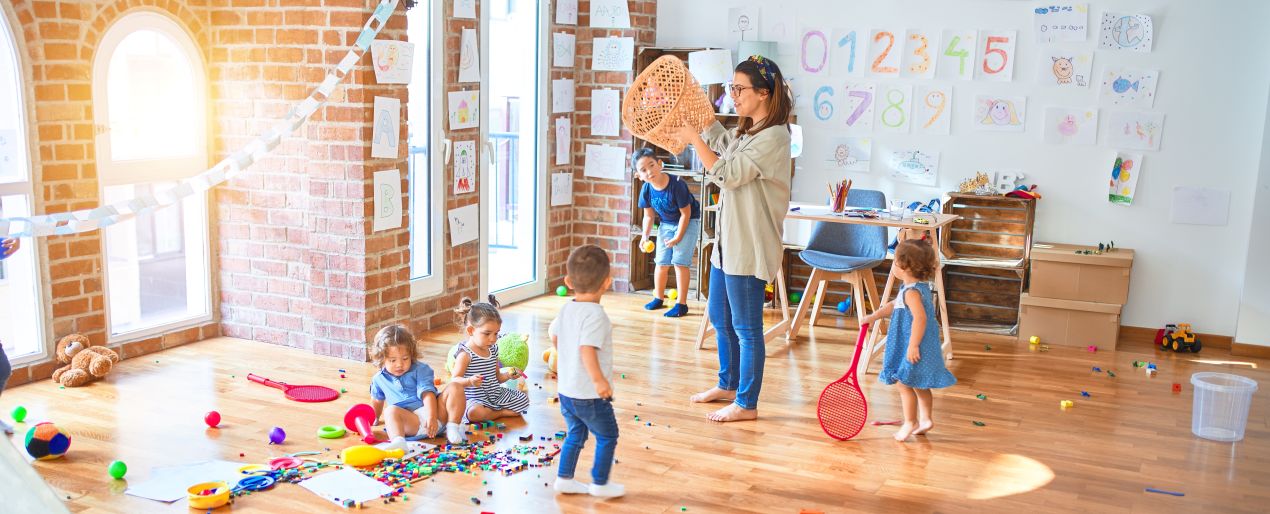 Erzieherin und Kinder in einem kreativen Kita-Raum mit Spielzeug und Zeichnungen – typische Szene fuer Quereinsteiger Kindergarten