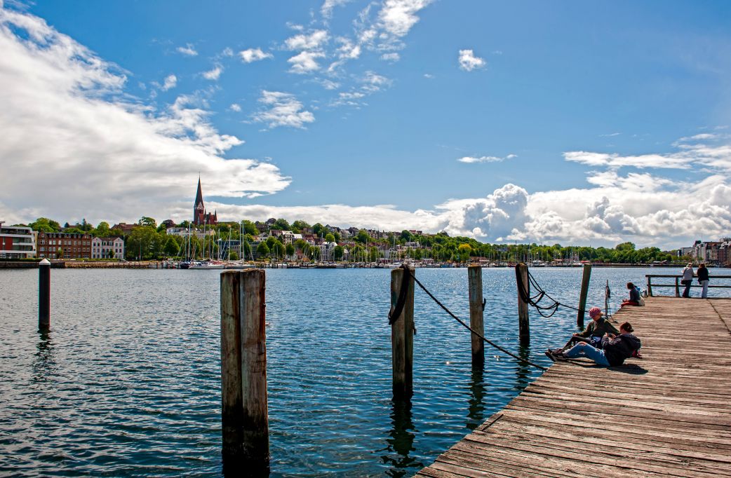 Veranstaltungen Flensburg – Menschen entspannen am Hafen bei sonnigem Wetter