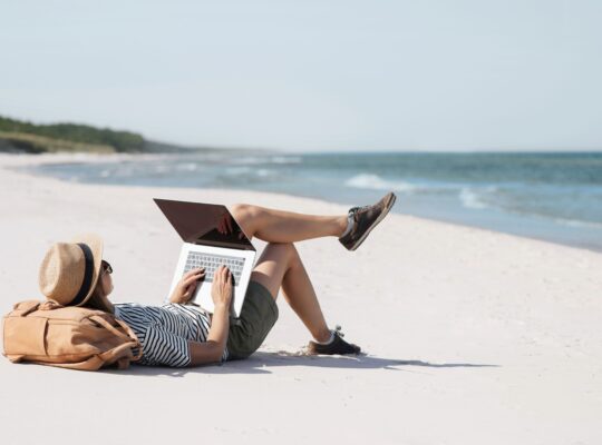 Eine Person liegt an einem Strand und tippt auf einer Laptop Tastatur