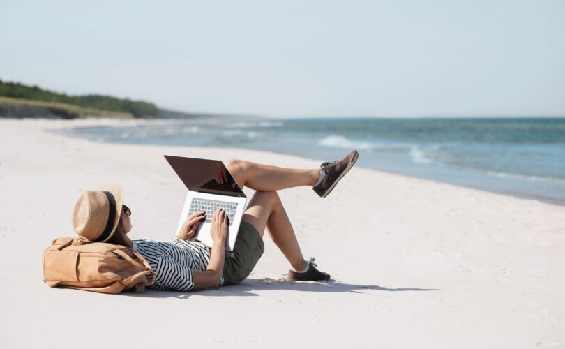 Eine Person liegt an einem Strand und tippt auf einer Laptop Tastatur
