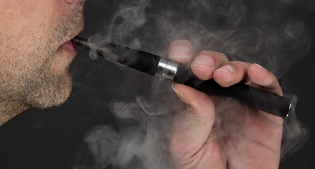Mann mit Dreitagebart nutzt kompakte E-Zigarette, dichter Dampf umgibt das Elfbar Liquids Geraet
