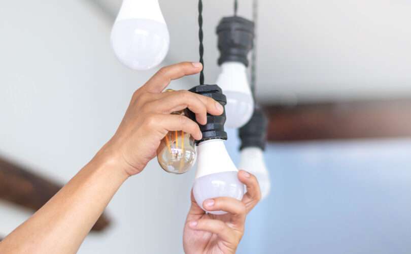 Konzept der Hauswartung, Energieeinsparung oder Elektroarbeiten. Hände wechseln eine Glühbirne an einer Deckenleuchte.