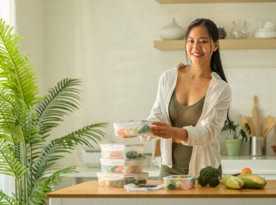 Attraktive Frau ordnet ihre Mahlzeiten-Behälter auf der Küchenarbeitsplatte, bereit für eine Woche gesunder Ernährung.